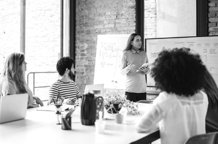 Man pointing at a whiteboard with a group of people around him