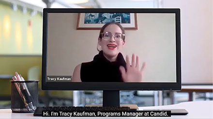 Tracy Kaufman waves as a video of her discussing grant proposal budgets plays on a computer screen on a desk.