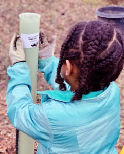 A girl pastes a label on a plastic pipe in a garden