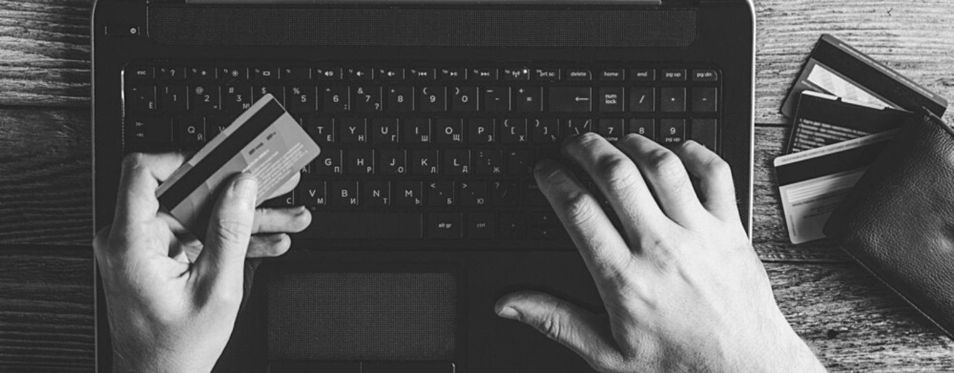 one hand types on computer keyboard, the other hand holds a credit card