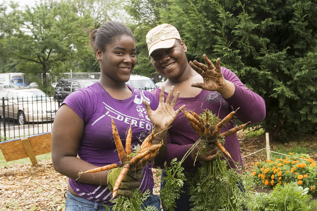 Two young Black women holding freshly picked carrots