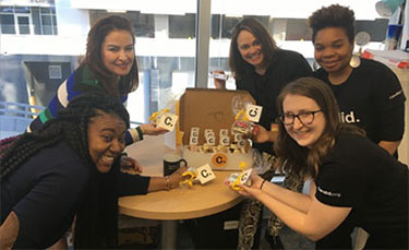 Five women from Candid's Atlanta all office celebrate Candid's first anniversary with cupcakes and by wearing black Candid T-shirts.