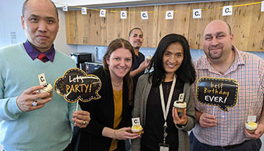 Three men and two women from Candid's NYC office celebrate Candid's first anniversary with cupcakes and signs.